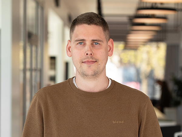 Kahala taustaga mees pruunis kampsunis seisab.