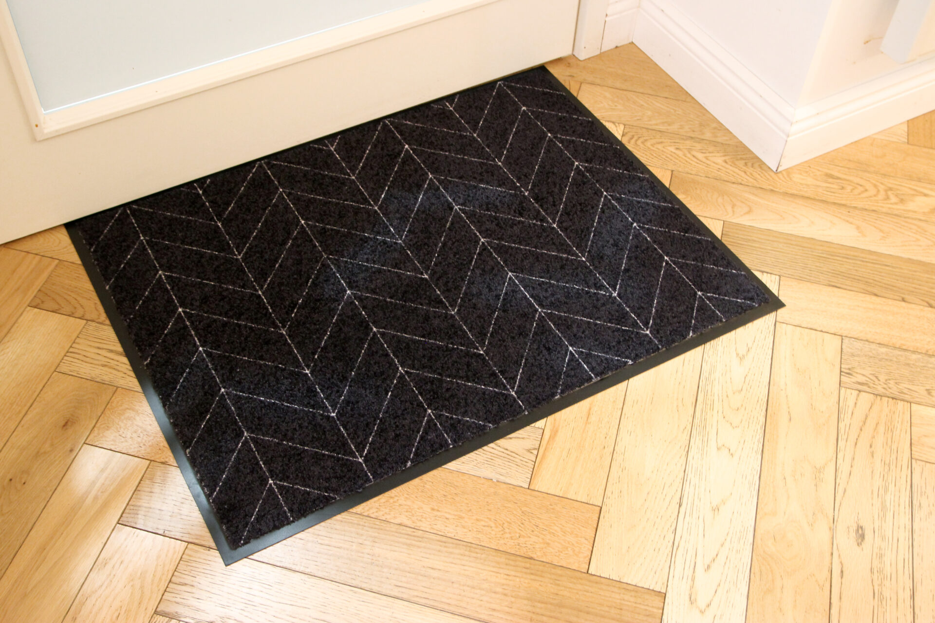 Tume uksematt kalatüüpi mustriga puitpõrandal