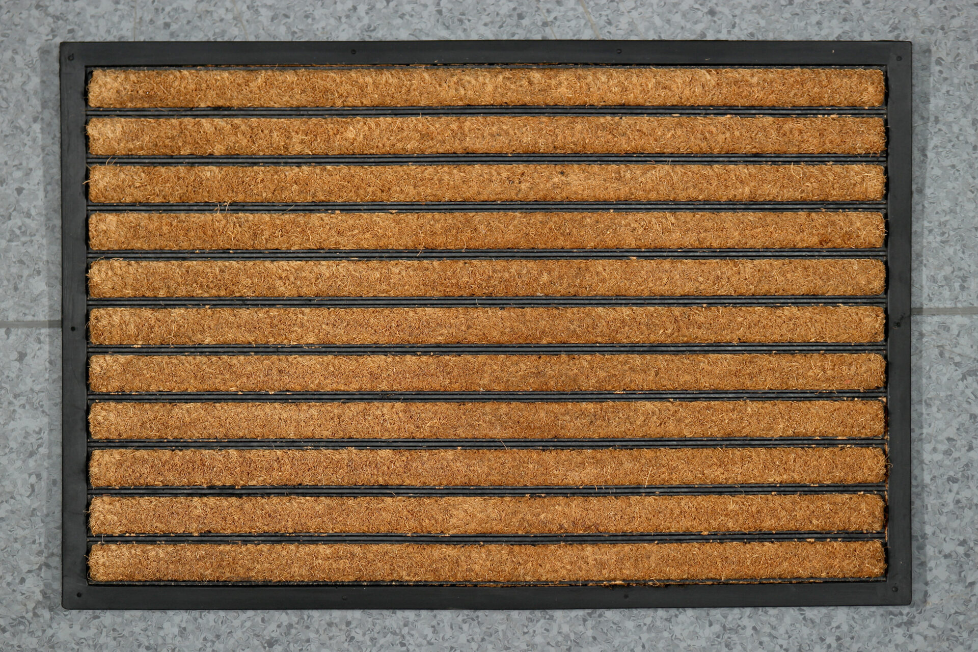 Pruuni ja musta vaip kivipõrandal välisukse ees