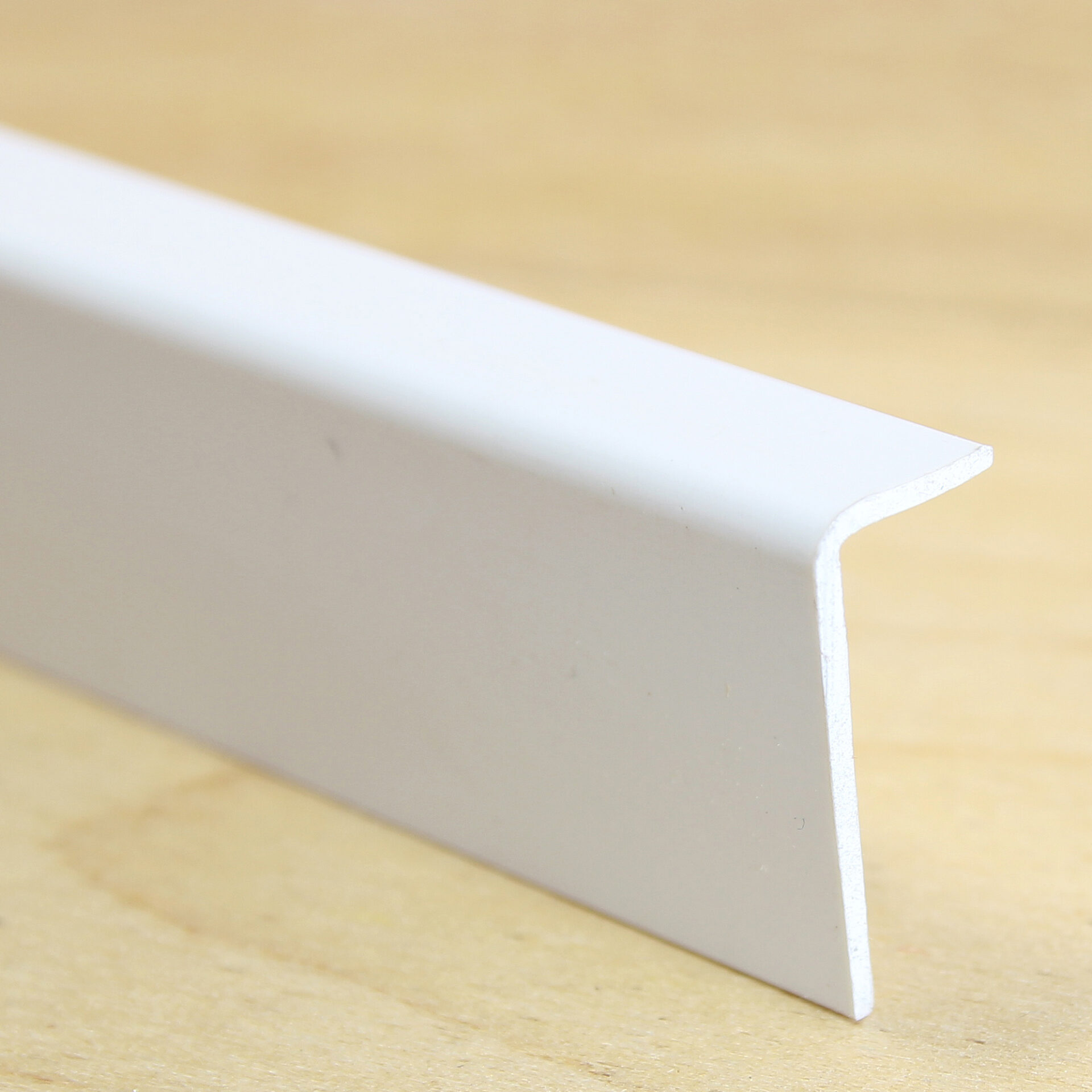 Valge plastist nurgaprofiil puidust taustal.